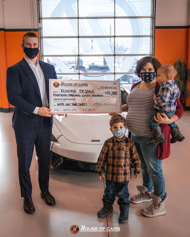 A 2021 Wipe Out Your Debt winner and her family with a House of Cars cheque for fourteen thousand eight hundred dollars.